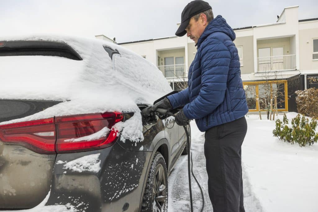 Beautiful view of a man connecting a charging cable to an electric car charging station on a frosty winter day.