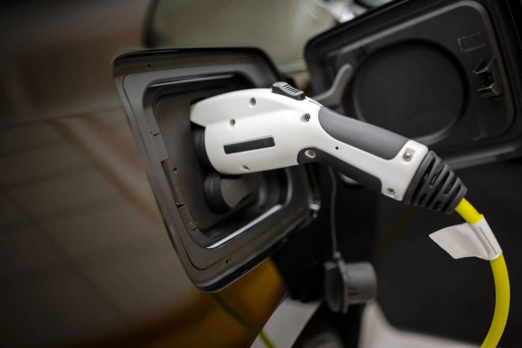 The electric car charger gun with power supply cable is inserted into the connector of the power supply unit of the refueling environmentally friendly car